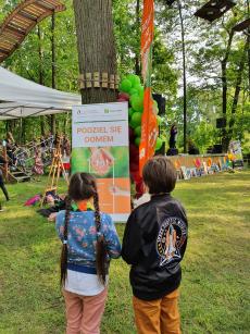 Powiększ zdjęcie: 1. Zdjęcie przedstawia dwoje dzieci w wieku siedmiu lat, chłopca i dziewczynę odwróconych tyłem zapatrzonych w pomarańczowo zielony plakat z napisem podziel się domem.