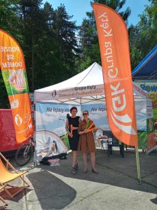 Powiększ zdjęcie: 2.	Zdjęcie przedstawia dwie kobiety stojące obok plakatu z napisem podziel się domem, promującym rodzicielstwo zastępcze, w tle pomarańczowe flagi z napisem Grupa Kęty.