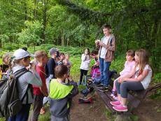 Powiększ zdjęcie: Grupa dzieci i młodzieży słucha instrukcji chłopca prowadzącego grę terenową w lesie