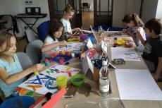 Powiększ zdjęcie: Grupa dzieci siedzi przy stole i maluje farbami.