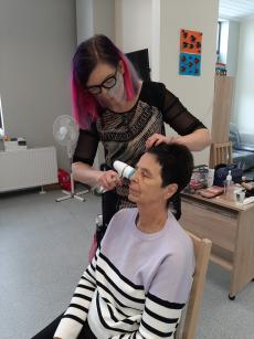 Powiększ zdjęcie: Seniorka z Klubu Senior Plus z ulicy Jutrzenki podczas zajęć z kosmetologiem poddaje się badaniu stanu skóry