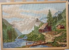Powiększ zdjęcie: Wyhaftowany pejzaż przedstawiający górski krajobraz oraz las i domki nad rzeką