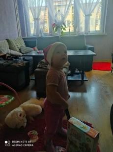 Powiększ zdjęcie: Zdjęcie przedstawia małe dziecko z czapką Mikołaja na głowie z zainteresowaniem spoglądającą na rozmówcę