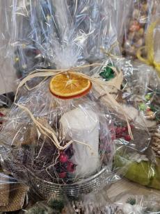 Powiększ zdjęcie: Zdjęcie przedstawia prezent świąteczny zawierający białą grubą świecę obok sztuczną żurawinę zapakowany w przeźroczysty celofan.