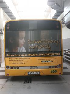 Powiększ zdjęcie: zdjęcie tyłu autobusu Miejskiego Zakładu Komunikacyjnego w Bielsku-Białej,  z widocznym plakatem  promującym  kampanię społeczną pod nazwą  „Szukam rodziny zastępczej” przedstawiający smutną dziewczynkę przy mokrym od deszczu oknie