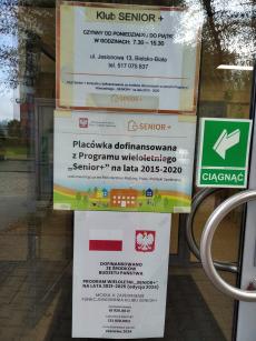 Powiększ zdjęcie: Drzwi wejściowe do Klubu Senior+ przy ul. Jesionowej 13 w Bielsku-Białej. Na górze drzwi plakat z białym tłem i pomarańczową ramką. Granatowymi literami napisano: Klub Senior+ czynny od poniedziałku do piątku w godzinach 7.30-15.30 ul. Jesionowa 13, 43-300 Bielsko-Biała, telefon 517 075 837. Klub Senior+ korzysta z dofinansowania ze środków otrzymanych w ramach Programu Wieloletniego „Senior+” na lata 2015-2020. Na dole logo Programu Senior+ czyli pomarańczowy domek z sercem. Poniżej na drzwiach plakat z godłem Polski i napisem: Ministerstwo Rodziny, Pracy i Polityki Społecznej oraz logo Programu Senior+ czyli pomarańczowy domek z sercem. Placówka dofinansowana z Programu Wieloletniego „Senior+” na lata 2015-2020 realizowanego przez Ministerstwo Rodziny, Pracy i Polityki Społecznej. Na dole plakatu kolorowy obrazek przedstawiający domki, drzewa, osoby siedzące przy stoliku i gimnastykujące się. Poniżej na drzwiach Plakat Informacyjny Programu SENIOR+, który przedstawia u góry flagę i godło Polski, poniżej napis: Dofinansowano ze środków budżetu państwa. Program Wieloletni „Senior+” na lata 2021-2025 edycja 2024. Moduł II – Zapewnienie funkcjonowania Klubu Senior+. Na dole plakatu napis: dofinansowanie 61 920,00 zł całkowita wartość 133 920,00 zł data podpisania umowy czerwiec 2024.